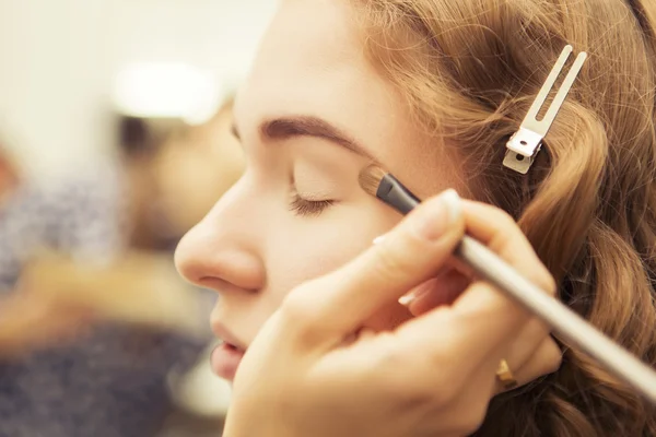 Morena maquillaje artista mujer aplicando maquillaje para un híbrido rubio —  Fotos de Stock