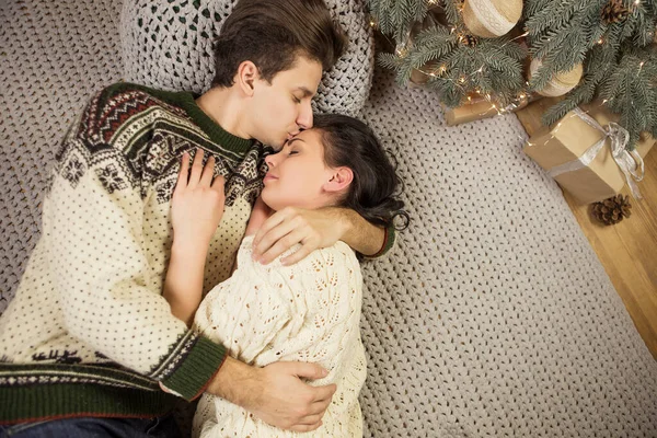 美しいブルネットの白人は クリスマスの新年の前夜にキャビンの居心地の良い暖かいセーターでカップルを愛し 笑顔でキスし お互いに楽しみを持っています 薄暗い暗い夜の光 トーン画像 — ストック写真