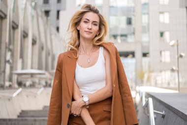 Güzel sarışın kadın, yüksek teknoloji iş binasının yanında, klasik şık, sıradan kıyafetlerle geziyor. Kahvesini fincana koyup yaz sıcağının tadını çıkarıyor. Metin için boşluk