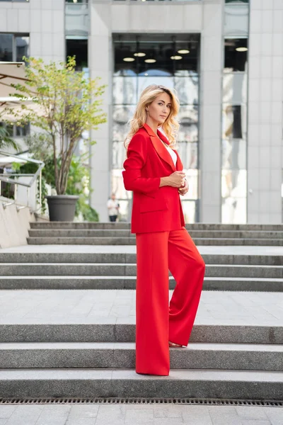 ハイテクビジネスビルの近くの屋外で赤の古典的なスマートカジュアル服の美しいブロンドの女性 テキストのスペース — ストック写真