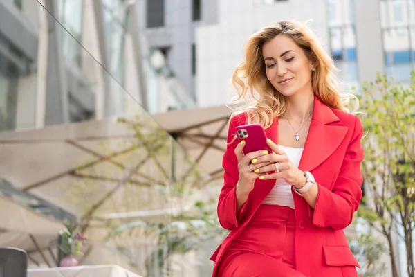 아름다운 금발의 여성이 야외에서 전형적 스마트 캐주얼 복장을 했습니다 휴대폰으로 — 스톡 사진