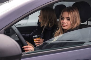 Arabadaki iki sarışın kız. Biri şoför, diğeri yolcu. Koyu soğuk sonbahar akşamı, kızlar palto giyer ve fincana gitmek için kahve içerler.