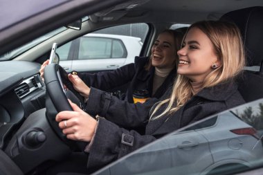 Arabadaki iki sarışın kız. Biri şoför, diğeri yolcu. Koyu soğuk bir sonbahar akşamı, kızlar palto giyer ve kahve içerek fincanlarını doldurur ve telefonlarında selfie çekerler.