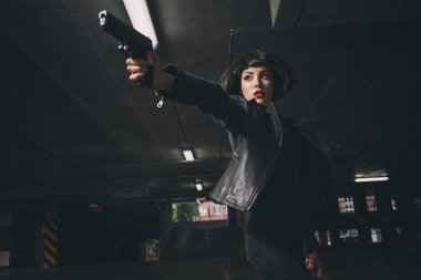 Güzel esmer, seksi ajan (katil ya da polis) Deri ceketli ve kot pantolonlu bir kadın, birinin peşinden koşuyor, onu park yerinde yakalamak için..