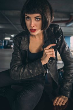 Güzel esmer, seksi ajan (katil ya da polis) Deri ceketli ve kot pantolonlu bir kadın, birinin peşinden koşuyor, onu park yerinde yakalamak için..