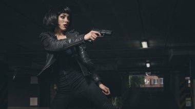 Güzel esmer, seksi ajan (katil ya da polis) Deri ceketli ve kot pantolonlu bir kadın, birinin peşinden koşuyor, onu park yerinde yakalamak için..