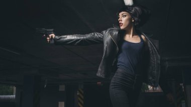 Güzel esmer, seksi ajan (katil ya da polis) Deri ceketli ve kot pantolonlu bir kadın, birinin peşinden koşuyor, onu park yerinde yakalamak için..