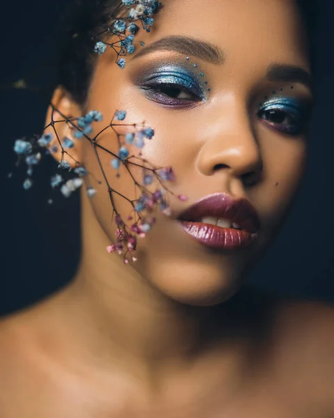 Dark skinned beautiful young woman posing sensually on a black background. Flawless skin with creative blue make up. Shallow depth of field portrait.