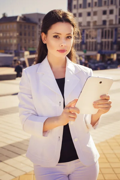 Schöne brünette Geschäftsfrau im weißen Anzug, die an einem Tab arbeitet — Stockfoto