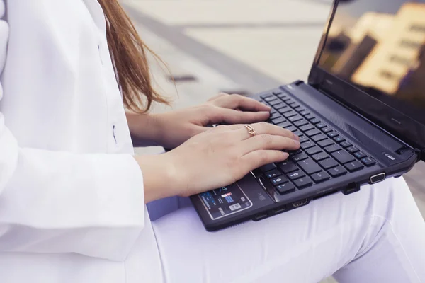 Beautiful brunette business woman in white suit with notebook on her lap, typing, working outdoors. Copy space — Stock Photo, Image