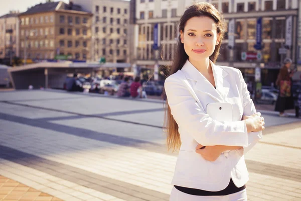 Beautiful brunette business woman in white suit with tablet in her hands outdoors. copy space — Stock Photo, Image