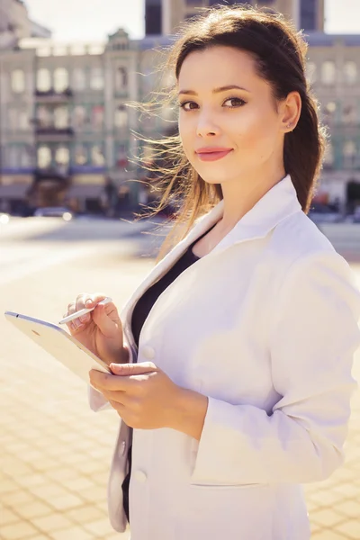 Belle femme d'affaires brune en costume blanc travaillant sur une tablette dans ses mains à l'extérieur — Photo