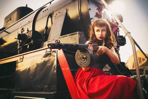 아름 다운 섹시 한 갈색 머리 복고풍 여자 핀-업 헤어스타일과 메이크업은 반바지에 셔츠 빈티지 기차에 그녀의 손에 있는 pca 총. 야외. 레트로 톤 — 스톡 사진