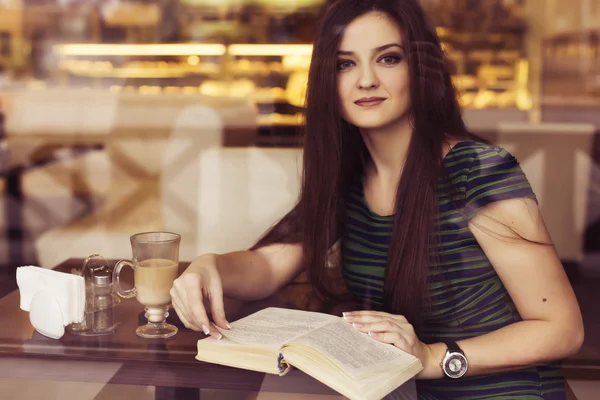 Mujer morena sentada en el café leyendo libro, tachonado y bebiendo café. Copiar espacio —  Fotos de Stock