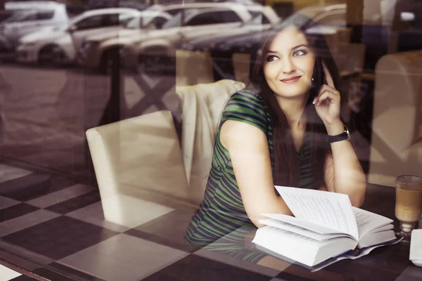 Femme brune assise au café lisant le livre, claquant et buvant du café et parlant au téléphone. Espace de copie — Photo