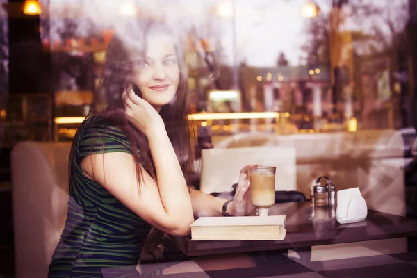 Brünette Frau sitzt im Café und liest Buch, stopft und trinkt Kaffee und telefoniert. Kopierraum — Stockfoto