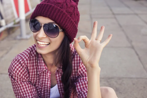 Menina adolescente morena em roupa hipster (calções de ganga, keds, camisa xadrez, chapéu) com um skate no parque ao ar livre — Fotografia de Stock