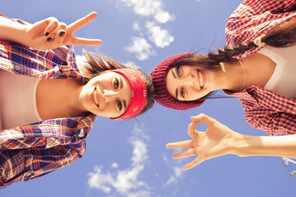 Two Brunette teenage girls friends in hipster outfit (jeans shorts, keds, plaid shirt, hat) with a skateboard at the park outdoors. — Stock Photo, Image