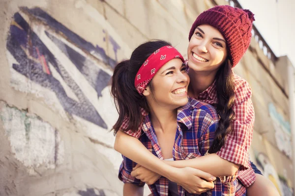 Two Brunette teenage girls friends in hipster outfit (jeans shorts, keds, plaid shirt, hat) with a skateboard at the park outdoors. Copy space — Stock Photo, Image