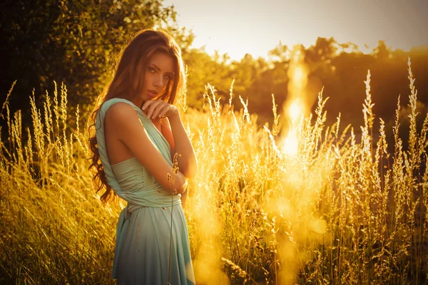 Hermosa rubia con un largo pelo rizado en un largo vestido de noche en movimiento al aire libre en la naturaleza en la puesta de sol de verano. Copiar espacio —  Fotos de Stock