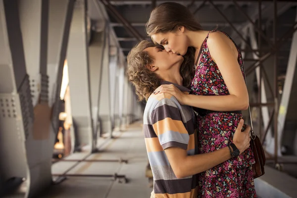 Young couple kissing in the summer daylight on a bridge construc — Stock Photo, Image