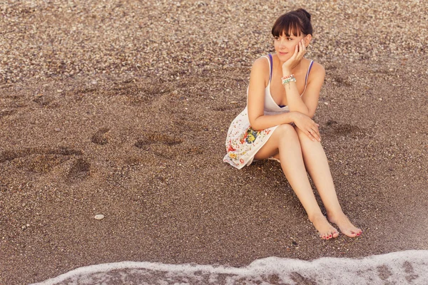 Mujer sentada en una playa de arena cerca del mar mirando el agua , —  Fotos de Stock