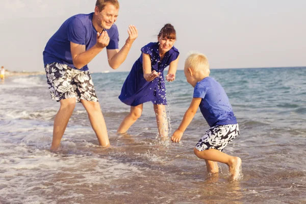 Familia de pie en una playa de arena cerca del mar jugando en el wate —  Fotos de Stock