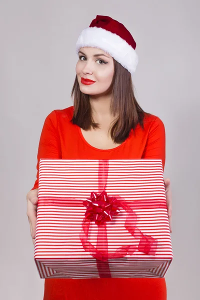 Esmer kadın kırmızı elbise ve Santa şapka hediye tutarak ve kamera arıyorum — Stok fotoğraf