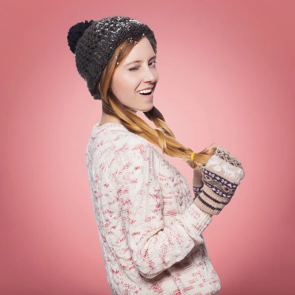 Mulher ruiva bonita em roupa de inverno: camisola quente, cachecol e chapéu com neve por toda parte. Isolado em vermelho rosa — Fotografia de Stock