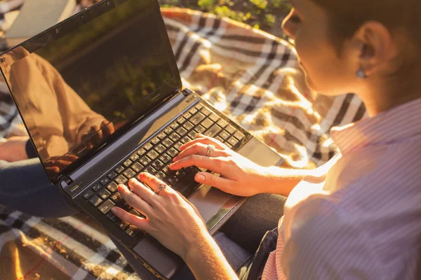 Beautiful brunette woman studying sitting on a plaid typing on a — Stock Photo, Image
