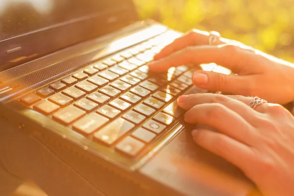 Mulher digitando em um teclado laptop em um dia ensolarado quente ao ar livre . — Fotografia de Stock