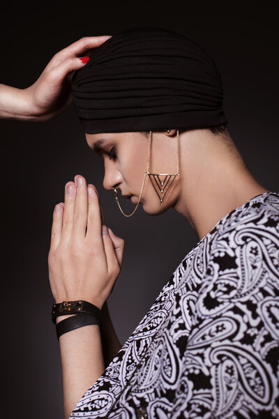 Young beautiful man in turban and with chains on his face prays 