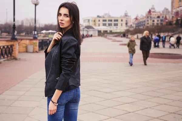 Hermosa mujer morena en chaqueta de cuero negro caminando sobre el —  Fotos de Stock