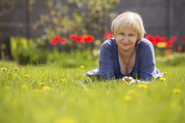 Beautiful blonde eldery senior woman relaxing on a grass in back — Stock Photo, Image