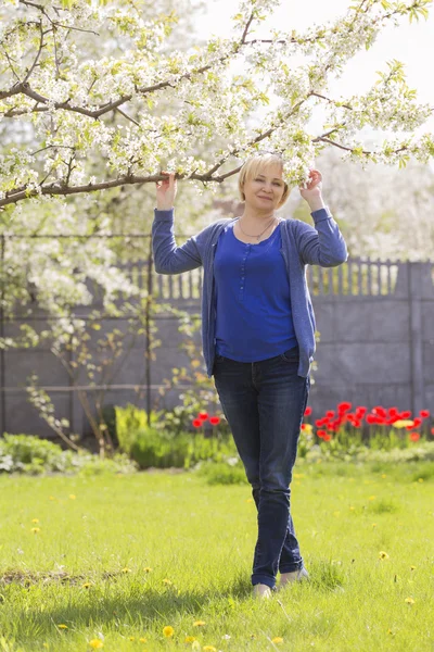 Beautiful blonde eldery senior woman relaxing on a grass in back — Stock Photo, Image