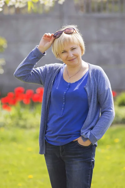 Beautiful blonde eldery senior woman relaxing on a grass in back — Stock Photo, Image