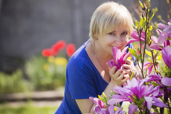 Beautiful blonde eldery senior woman relaxing on a grass in back — Stock Photo, Image