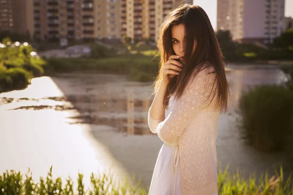 Young beautiful brunette girl in white dress standing near river — Stock Photo, Image