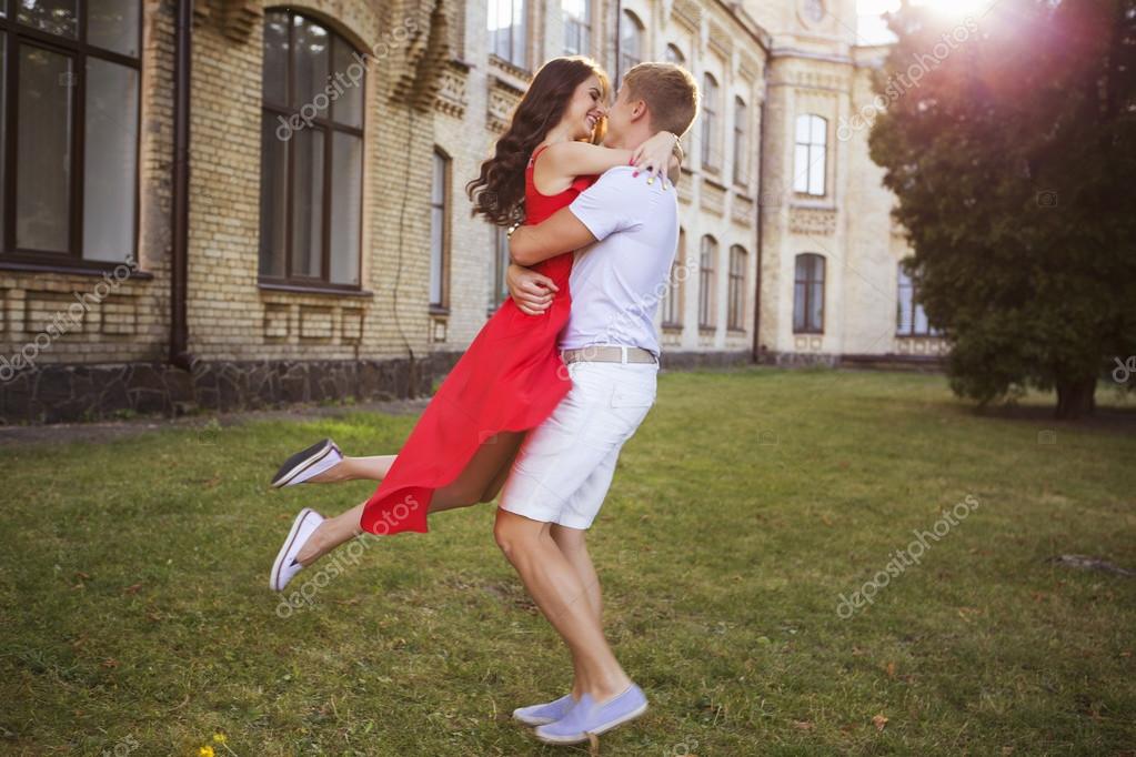 Beautiful brunette couple in love hugging on a date in the park. She in red  dress,