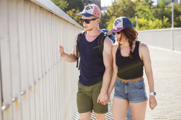 ショート パンツとバックパックが夏の日の都市の周り旅行を歩いて手を繋いでいるカップル — ストック写真