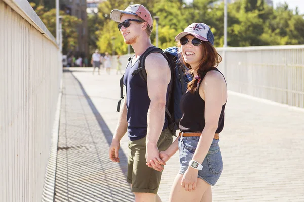 Couple en short et avec un sac à dos tenant la main se promenant dans la ville en journée d'été — Photo