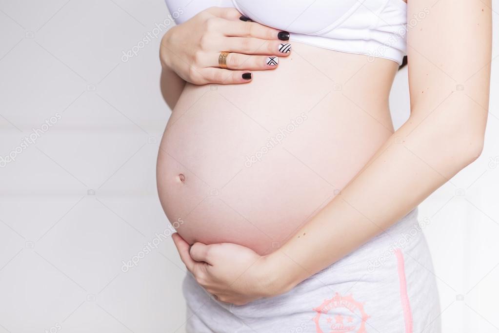 Pregnant caucasian white woman standing in white bra and shorts,