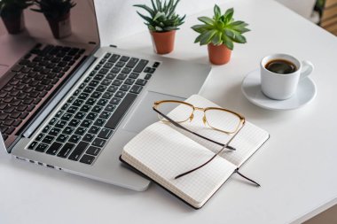 Masanın üzerinde bir dizüstü bilgisayar var. Yakınlarda açık bir günlük dolanıyor ve bardaklar yerde.