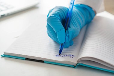 Eldivendeki kadın eli deftere yazıyor. Coronavirus 19 (covid-19)