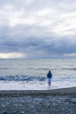 Kız, fırtına sırasında sırtı deniz kıyısında durur.
