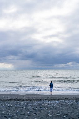 Kız, fırtına sırasında sırtı deniz kıyısında durur.