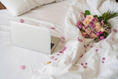 Yatağın üzerinde bir dizüstü bilgisayar var, yanında da bir buket çiçek.