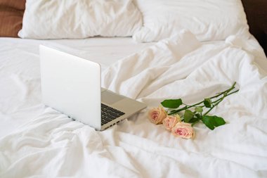 Yatağın üzerinde bir dizüstü bilgisayar var, yanında da bir buket çiçek.
