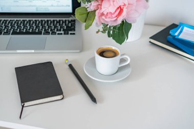 Masanın üzerinde bir laptop, yanında bir kupa kahve ve bir günlük var.