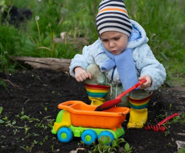 Parlak elbiseli çocuk, bahçedeki siyah toprakta oyuncak bir kamyonla oynuyor.
